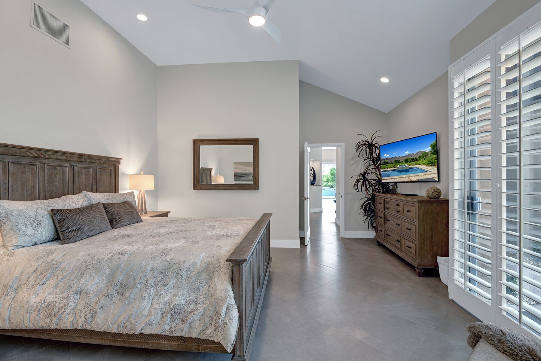 Une chambre avec un grand lit, une commode, un téléviseur et une vue sur une piscine par la fenêtre.