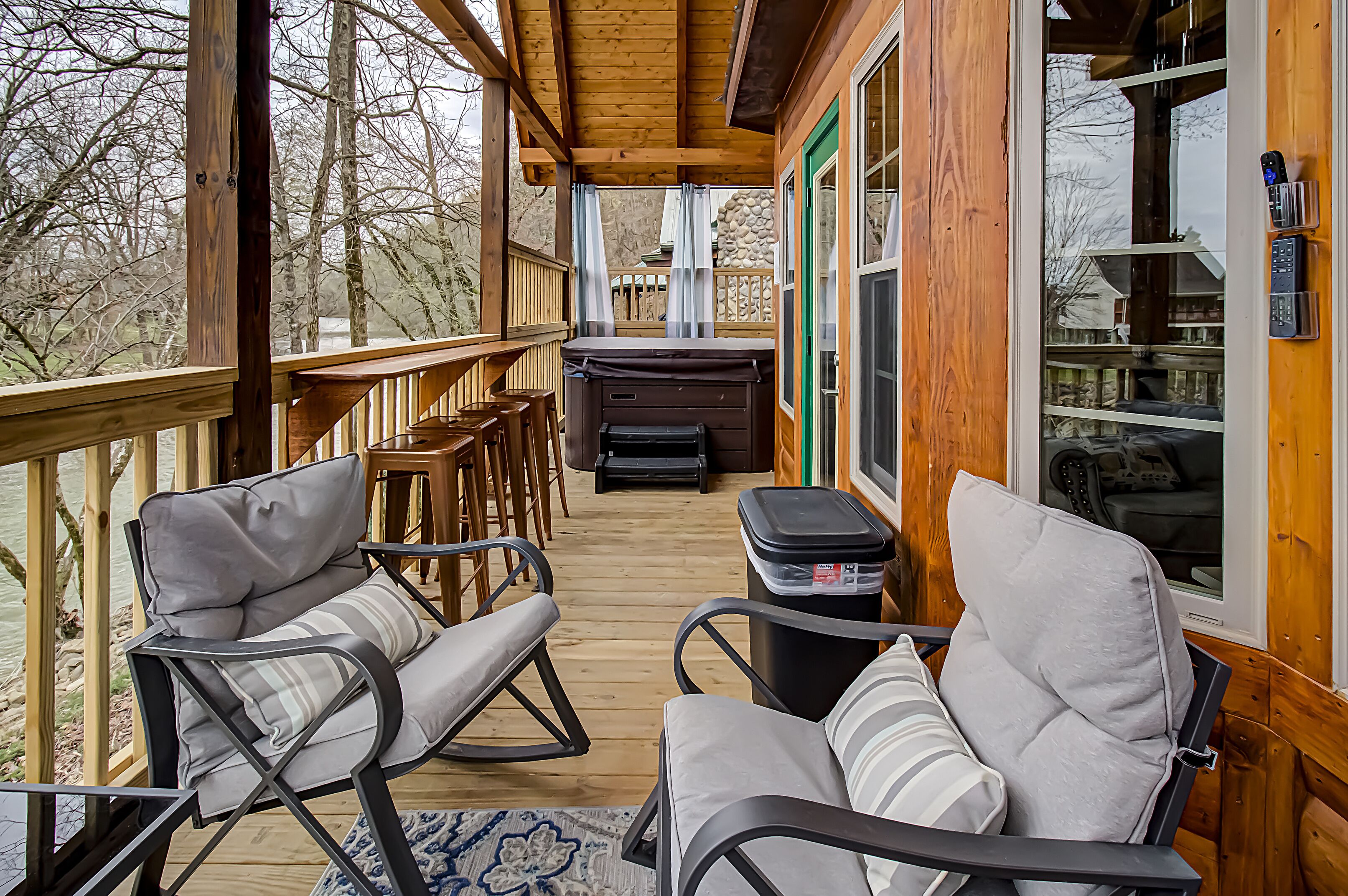 A wooden deck with two rocking chairs, a small table, and a trash can.