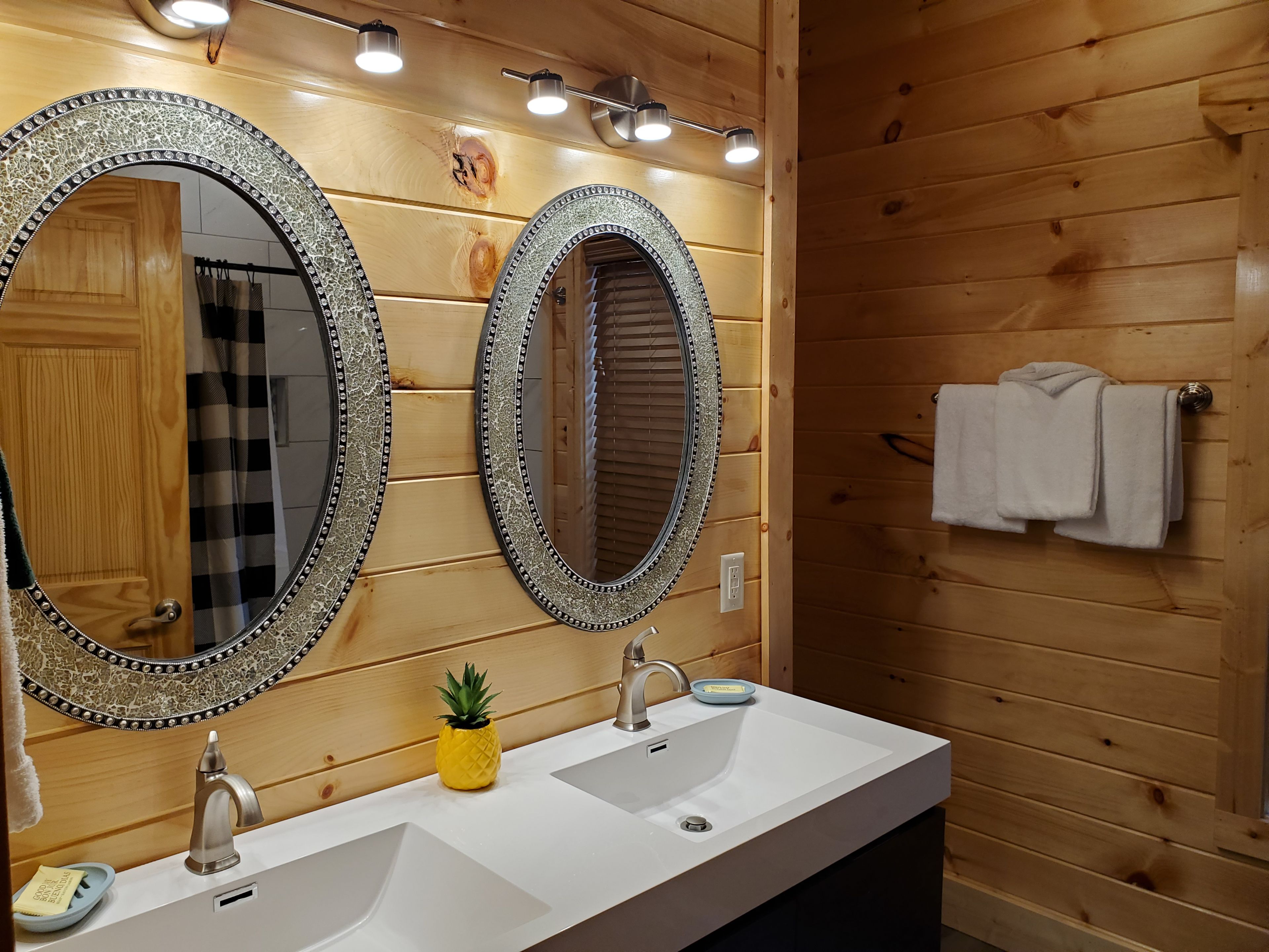Een badkamer met twee grote spiegels, houten wanden, een wastafel met kraan en een handdoekhouder.
