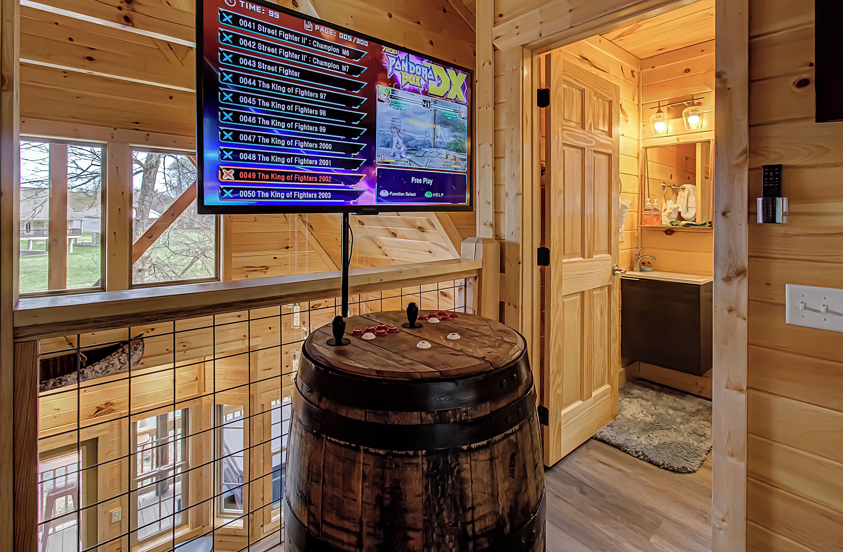 A wooden interior with a mounted screen displaying a game menu, a wooden barrel, and a view of the outside.