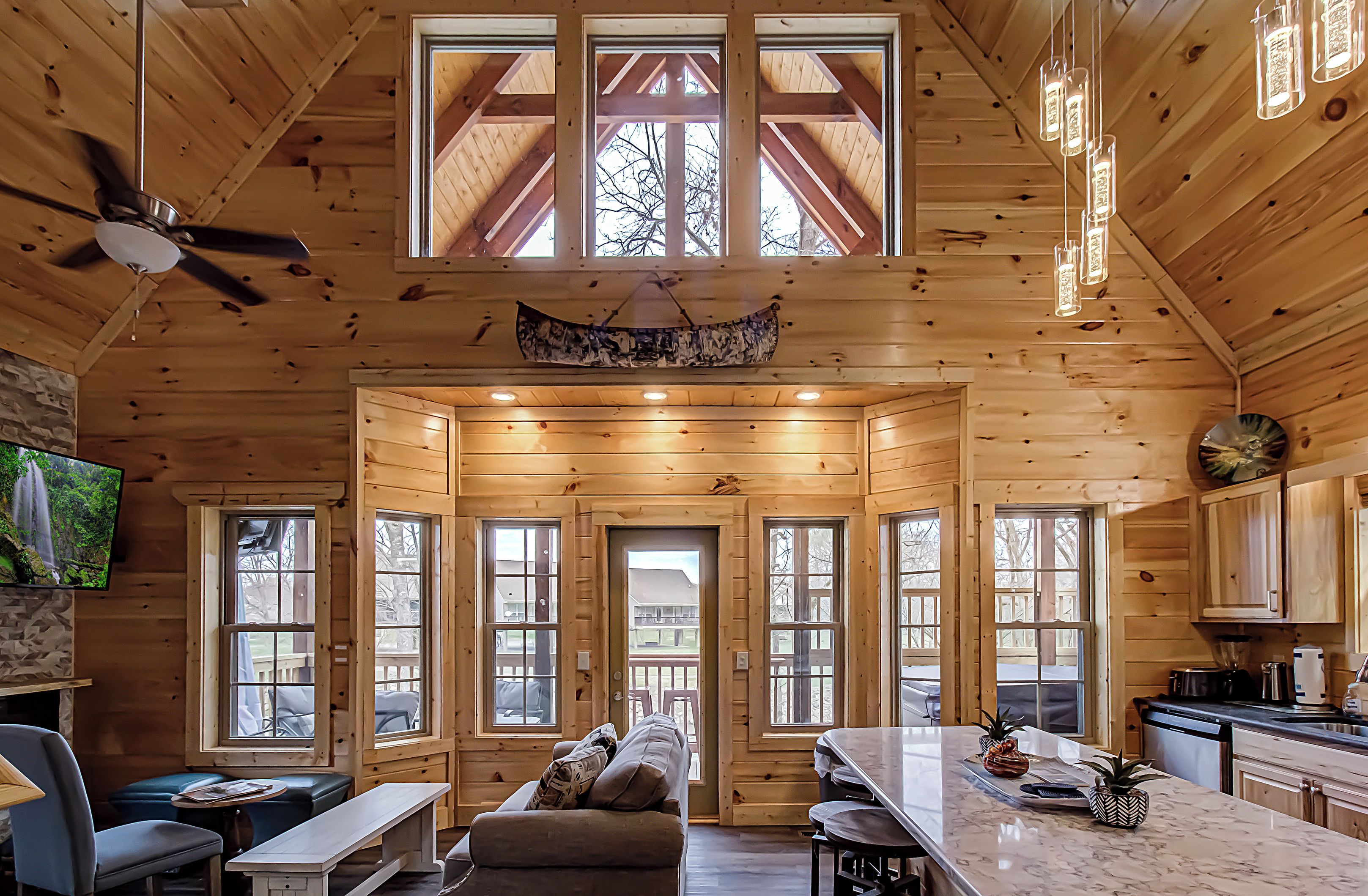 A spacious cabin with a high ceiling, large windows, a dining area, and a kitchen.