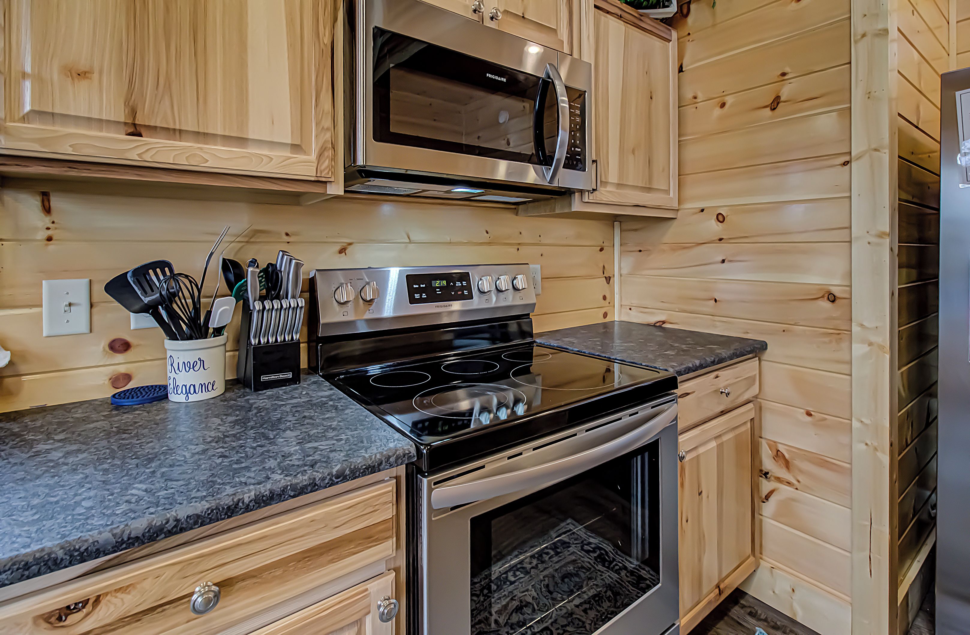 Una cocina con armarios de madera, estufa de acero inoxidable, microondas y un juego de cuchillos y utensilios.