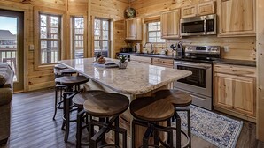 A wooden cabin kitchen with a large island, bar stools, stainless steel appliances, and wooden cabinets. - River View | Pigeon Forge  | Arcade | Hot Tub | WiFi | Fireplace (Pigeon Forge)