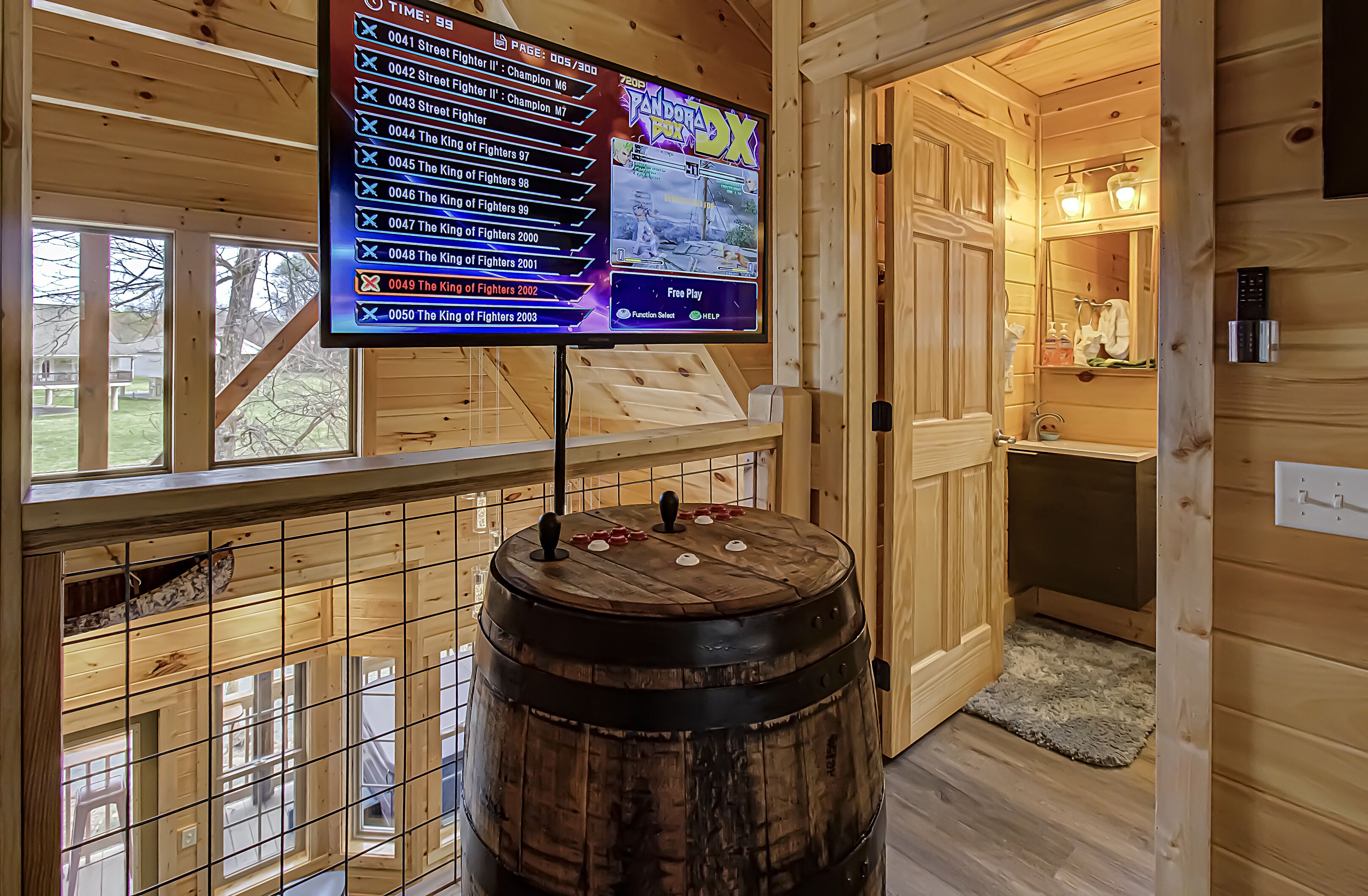 A wooden interior with a mounted screen displaying a game menu, a wooden barrel, and a view of the outside.