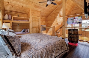 A wooden cabin with a bed, a TV, and a barrel.