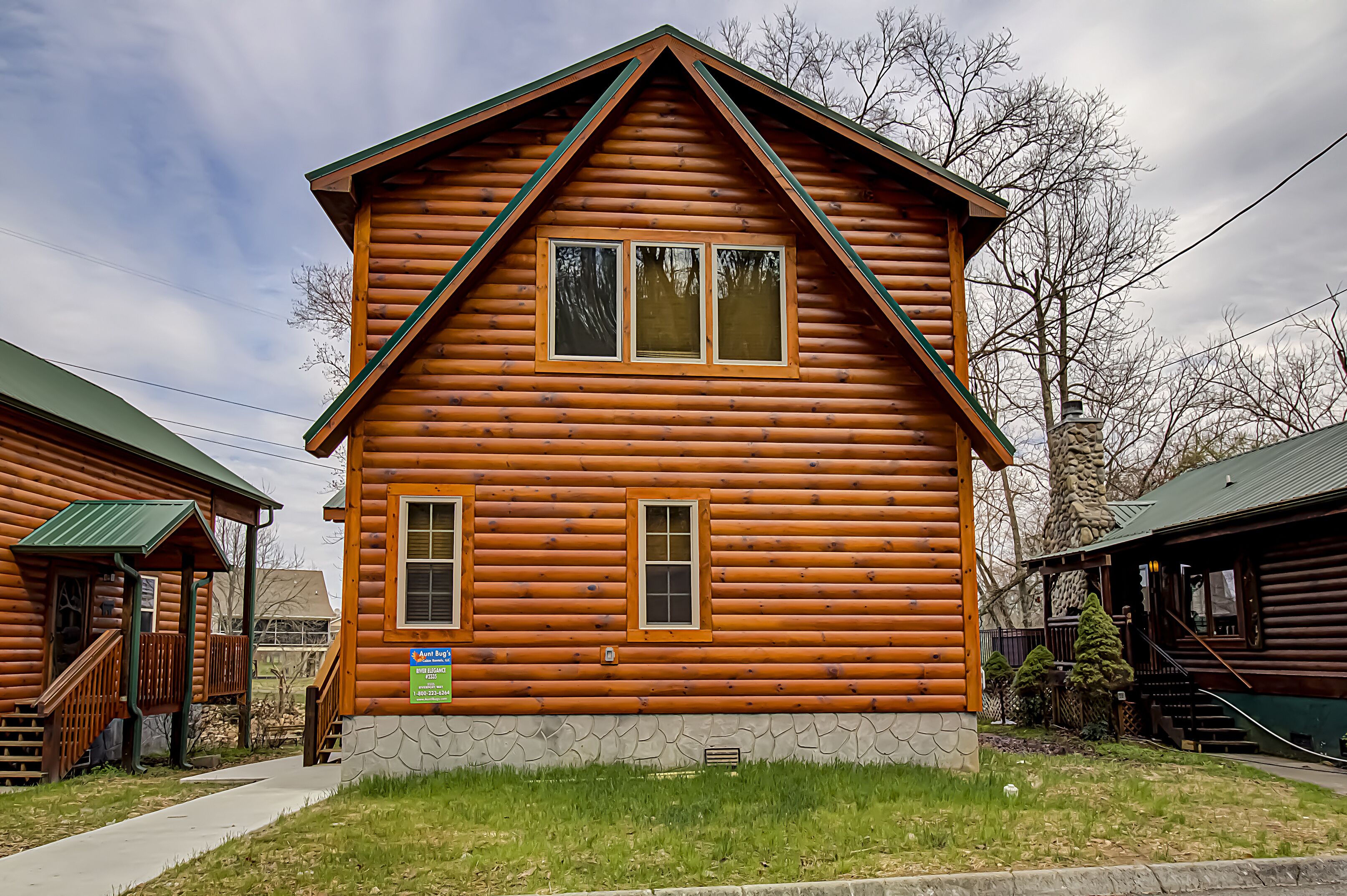 A log cabin with a gabled roof, two windows, and a stone foundation.