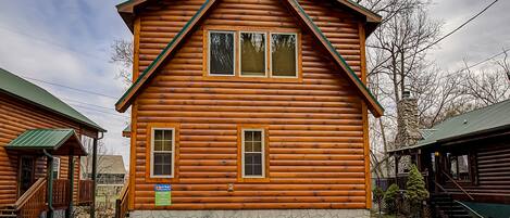 A log cabin with a gabled roof, two windows, and a stone foundation.