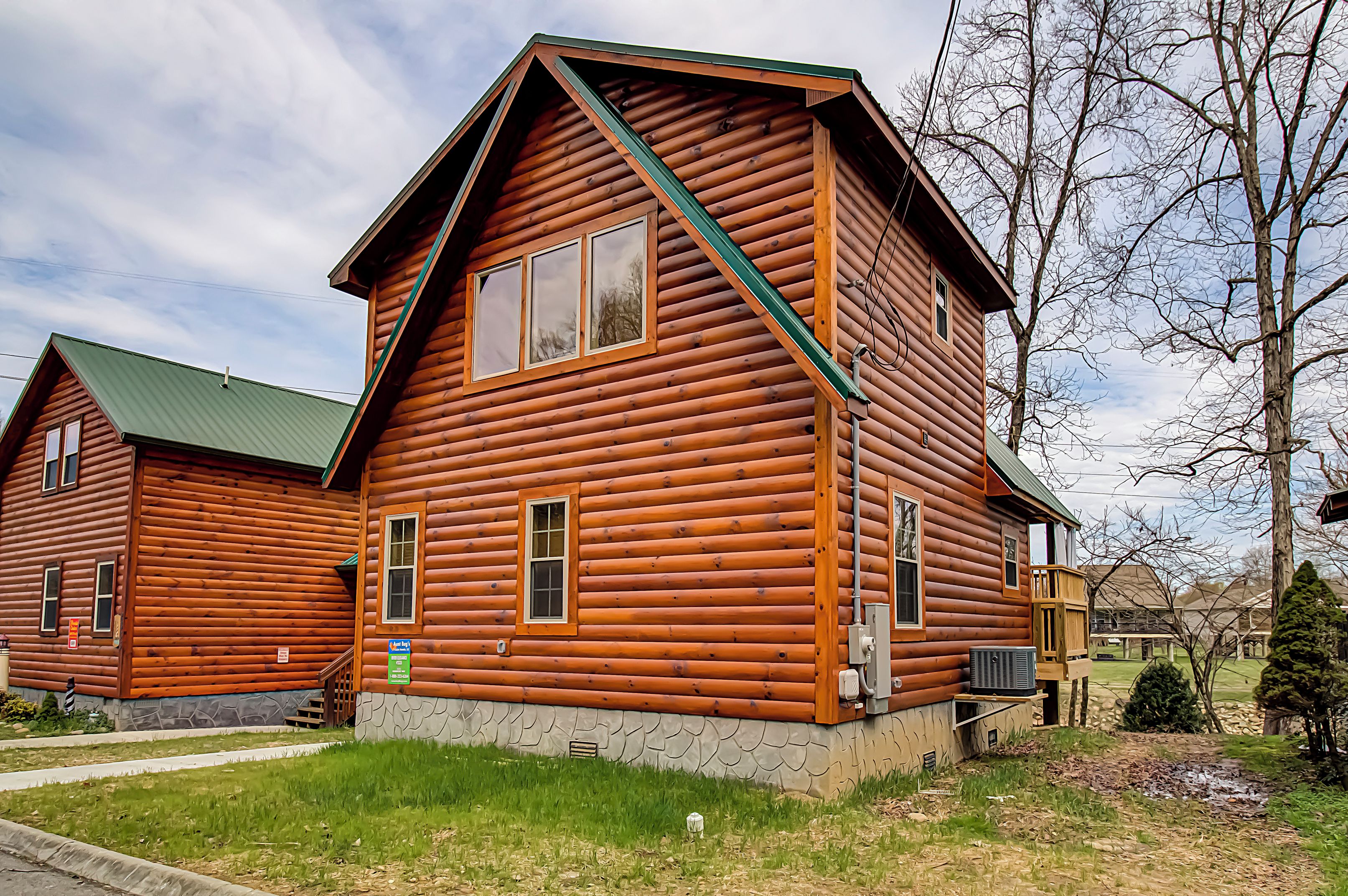A log cabin with a green roof, a stone foundation, and a small porch.