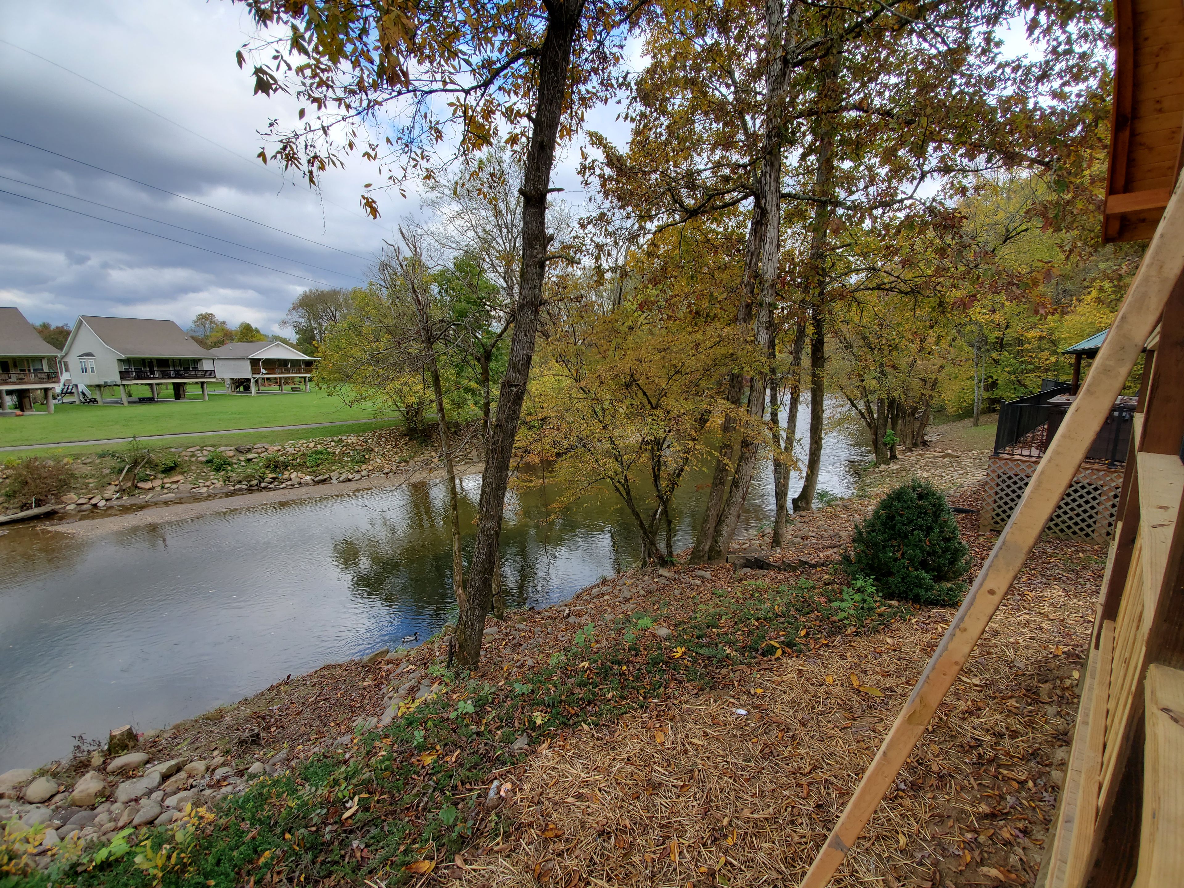 Blick auf einen Fluss mit einer Holzterrasse, die auf ruhiges Wasser blickt, umgeben von Bäumen im Herbstlaub.