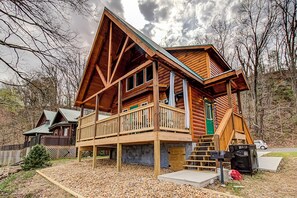 Une cabane en rondins avec une terrasse en bois, une porte verte et un petit porche.