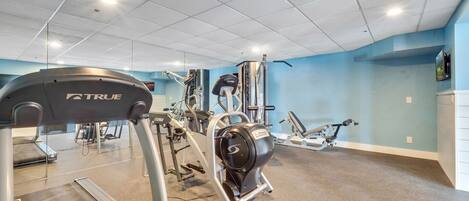 Et fitnesscenter med forskellig træningsudstyr, herunder løbebånd og vægtmaskiner, under et loft med indbyggede spots.