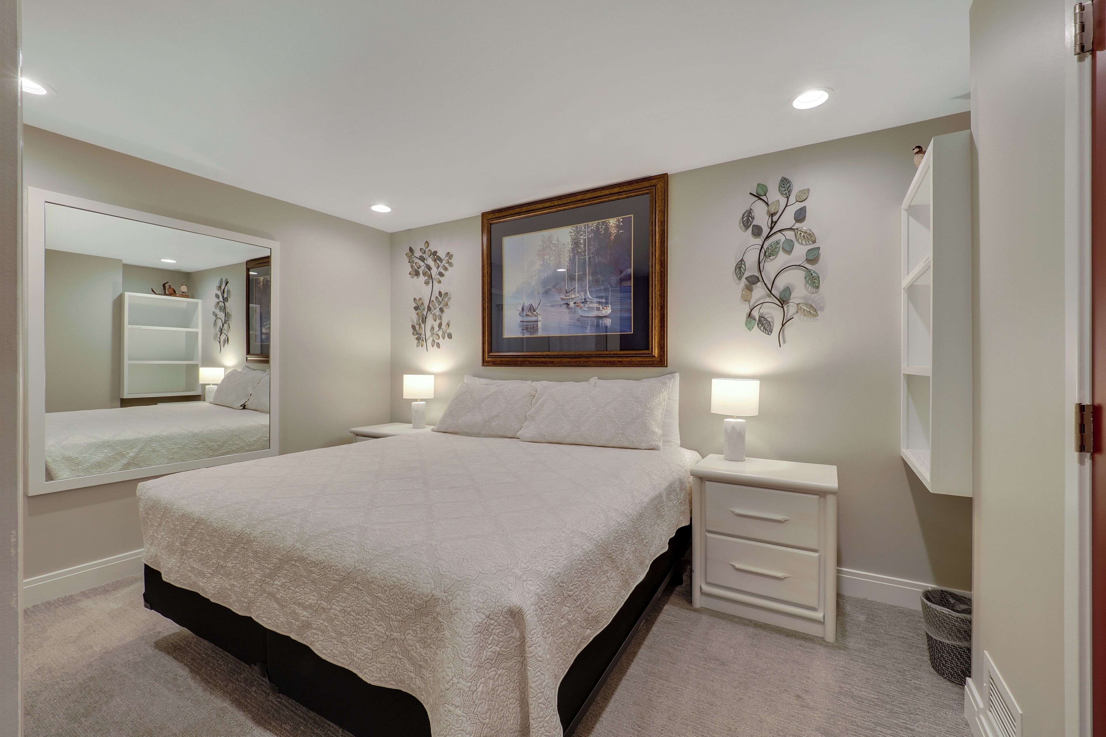 Un dormitorio con una cama grande, mesitas de noche, un espejo y decoración en la pared.