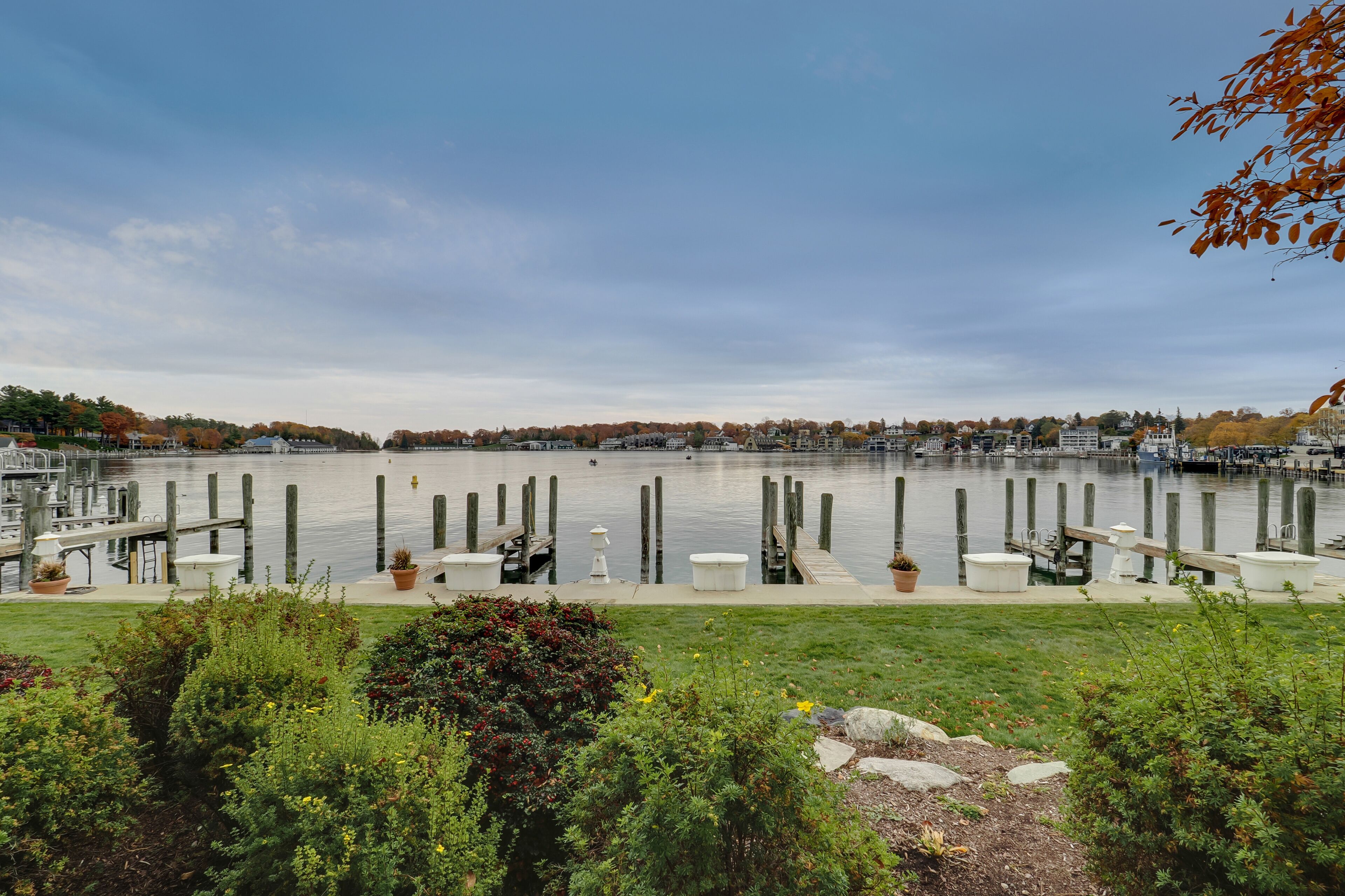 Une jetée au bord de l’eau, agrémentée de bancs et de plantes en pot, entourée de verdure et bordée d’un lac paisible.