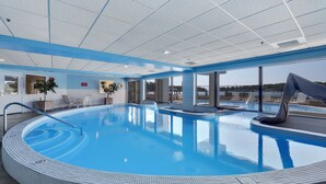 En stor inomhuspool med kakelbeklädd kant, ett avkopplingsområde med stolar och utsikt över omgivningen.