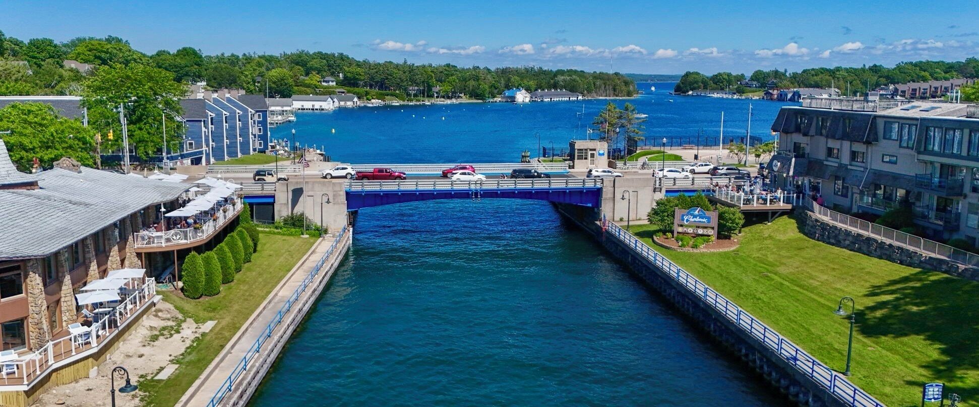 A waterfront hotel with a bridge connecting to a dock, a pool, and a sign for a nearby restaurant.