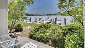 A view from a covered deck overlooking a lake with boats docked at the pier, surrounded by greenery and a clear sky.