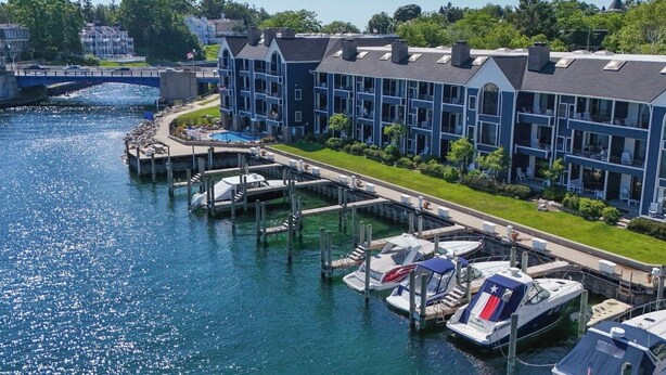 A waterfront hotel with multiple balconies, a dock with boats, and a bridge in the background.