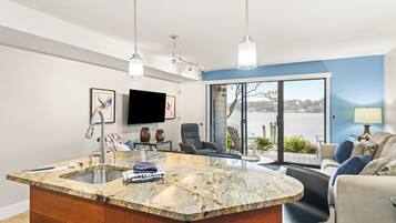 A modern kitchen with a large island, a flat-screen TV, and a dining area with a view of the water.