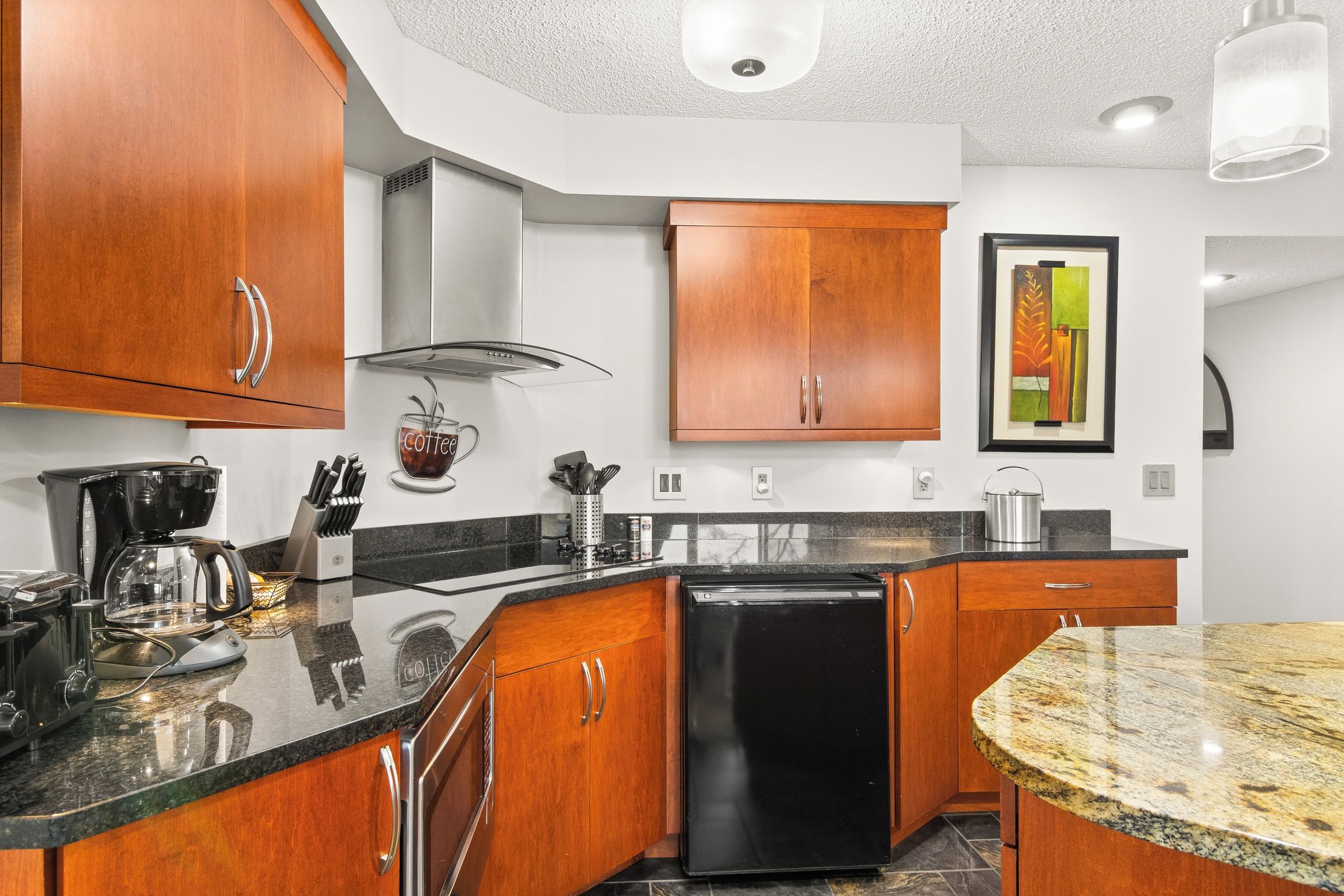 A modern kitchen with wooden cabinets, a black dishwasher, and a granite countertop.