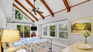 A bedroom with a bed, a ceiling fan, a TV, and large windows with shutters. - Walk to Beach | Private Pool | Pet Friendly (Hilton Head Island)