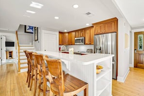 A modern kitchen with wooden cabinets, a central island with bar stools, stainless steel appliances, and a staircase leading to another level.