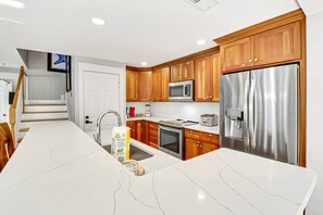 A modern kitchen with a central island, stainless steel appliances, wooden cabinets, and a white marble countertop.