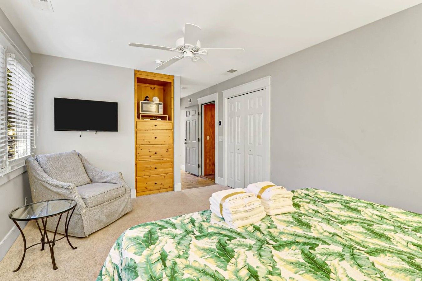 A bedroom with a bed, a chair, a TV, a wardrobe, and a ceiling fan.