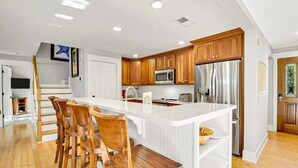 A modern kitchen with wooden cabinets, stainless steel appliances, and a central island with bar stools. - Walk to Beach | Private Pool | Pet Friendly (Hilton Head Island)