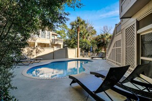 A swimming pool with lounge chairs, surrounded by trees and a building with a balcony.
