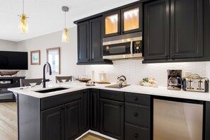 A modern kitchen with dark cabinetry, a stainless steel microwave, and a coffee maker. - 112 EWI Lake Charlevoix View Condo | Pool, Hot Tub, Sauna | Fireplace (Charlevoix)