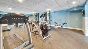Un gimnasio con diversos equipos de ejercicio, incluyendo cintas de correr y máquinas de pesas, bajo un techo con iluminación empotrada.