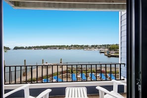 A balcony with a view of a calm body of water, a dock with boats, and a row of blue lounge chairs. - 112 EWI Lake Charlevoix View Condo | Pool, Hot Tub, Sauna | Fireplace (Charlevoix)