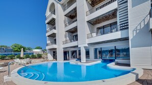 A modern building with a swimming pool, outdoor seating, and balconies. - Edgewater #119 | Water Views + Private Balcony | Pool, Hot Tub, Sauna | Patio (Charlevoix)