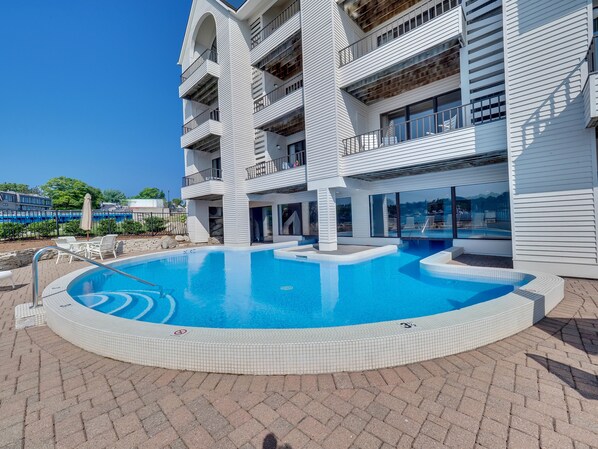 A modern building with a swimming pool, outdoor seating, and balconies. - Edgewater #119 | Water Views + Private Balcony | Pool, Hot Tub, Sauna | Patio (Charlevoix)