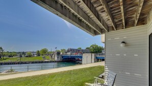 A view from a balcony overlooking a river with a bridge, a grassy area, and a building with a white exterior. - Edgewater #119 | Water Views + Private Balcony | Pool, Hot Tub, Sauna | Patio (Charlevoix)