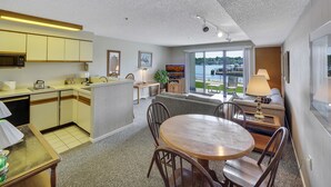 A modern kitchen with a dining area, large windows with a view of a body of water, and a balcony. - Edgewater #119 | Water Views + Private Balcony | Pool, Hot Tub, Sauna | Patio (Charlevoix)