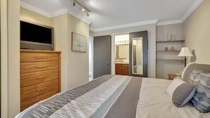 A hotel room with a bed, a wooden dresser, a television, a mirror, and a bathroom visible through an open door. - 223 Edgewater Inn | Pool, Hot Tub, Sauna | Cozy 1 BR Condo (Charlevoix)
