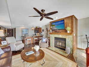 A modern living room with a fireplace, a television, and a ceiling fan. - 224 Edgewatern Inn | Waterfront Condo | Amazing Views | Pool, Hot Tub, Sauna (Charlevoix)
