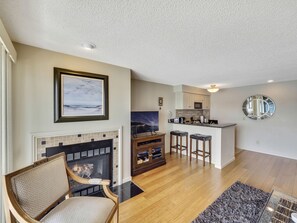 A living room with a fireplace, a dining area, and a kitchen with a bar.
