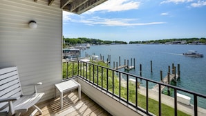A balcony with a view of a lake, docked boats, and a distant shoreline. - 227 Edgewater Inn | Private Lakefront Balcony | Pool, Hot Tub, Sauna (Charlevoix)