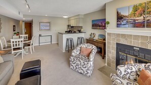A living room with a fireplace, a dining area, and a kitchen. - 228 Edgewater Inn | Peaceful Lake Charlevoix Escape | Pool, Hot Tub, Sauna (Charlevoix)