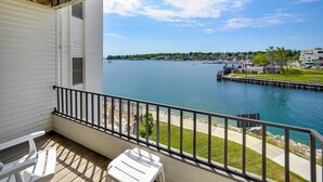 A balcony with a view of a calm lake, a dock, and a marina with boats. - 235 Edgewater | Scenic One-BDRM | Downtown Charlevoix | Pool, Hot Tub, Sauna (Charlevoix)