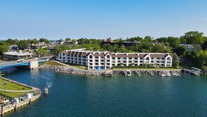 A waterfront hotel with multiple balconies, a swimming pool, and a dock with boats. - 239 Edgewater | Waterfront Views | Downtown Charlevoix | Pool, Hot Tub, Sauna (Charlevoix)
