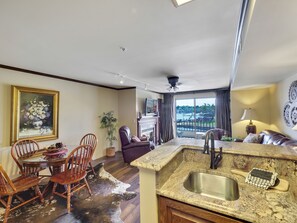 A modern kitchen with a granite countertop, stainless steel sink, and a dining area with wooden chairs and a table. - 240 Edgewater | On Gorgeous Lake Charlevoix | Downtown | Pool, Hot Tub, Sauna (Charlevoix)
