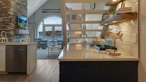 Une cuisine moderne avec un mur d’accent en pierre, un grand îlot central et une vue dégagée sur l’extérieur grâce à une porte en arc de cercle.