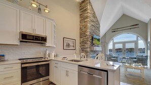 Une cuisine moderne avec des meubles blancs, des appareils en acier inoxydable et un mur d’accent en pierre.