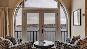 Une pièce dotée d’une grande fenêtre en arc de cercle donnant sur un plan d’eau, de deux fauteuils à motifs et d’une petite table ronde.
