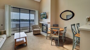 A living room with a sofa, a coffee table, a fireplace, a dining table with chairs, a TV, and a view of the water. - 347 Edgewater | 3rd Floor Balcony | Downtown Chx | Pool, Hot Tub, Sauna (Charlevoix)