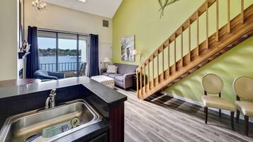 A modern living room with a kitchen area, a staircase, and a view of the sea.