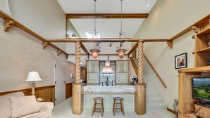 Een ruime woonkamer met een houten trap, een keuken met een centraal eiland, en een gezellige zithoek met een bank en een bijzettafeltje.